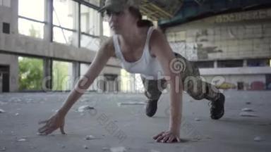自信<strong>坚强</strong>的年轻女子穿着军装，俯卧撑在一个荒芜的工厂里。 高跟鞋躺在前台